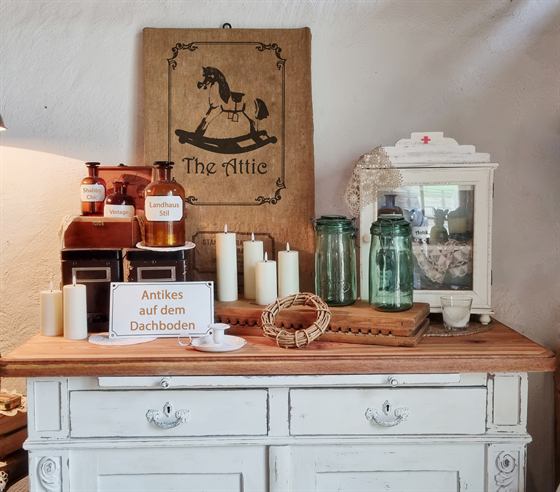 Weiße Anrichte mit Apothekerflaschen, Kerzen und dem Jute-Banner von The Attic