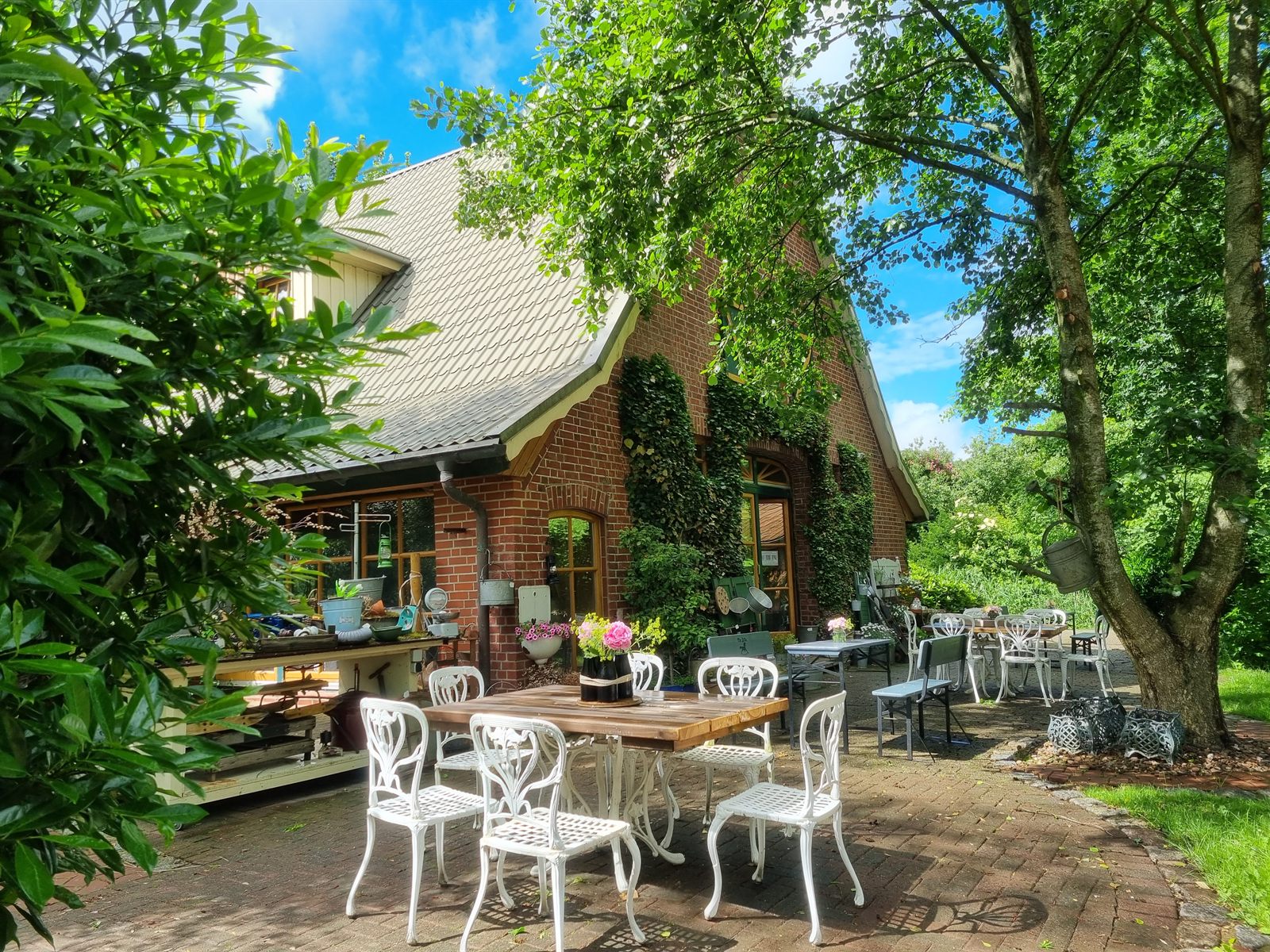 Altes Backstein-Bauernhaus mit Gartencafé-Tischen unter Bäumen – der Sitz von The Attic in Ihlienworth